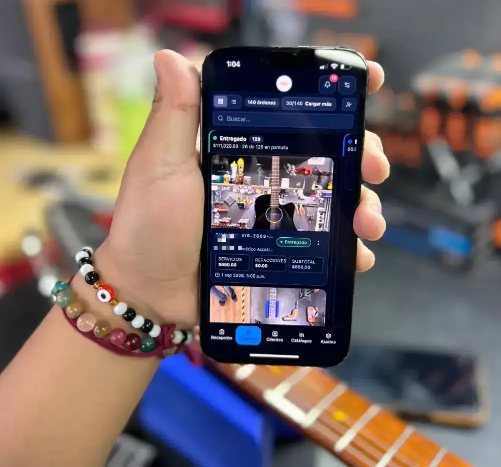 Un teléfono con el tablero de BujiOps abierto, sostenido dentro de un taller de instrumentos, con 140 órdenes y $111,020 entregados